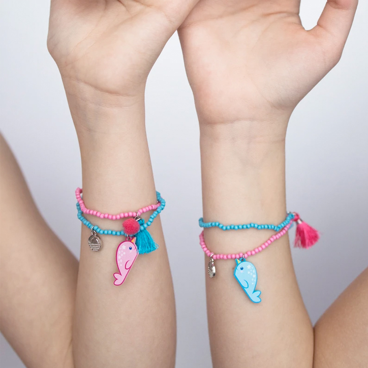 Two girls holding up their arms to show off their Calico Sun narwhal best friend charm bracelets