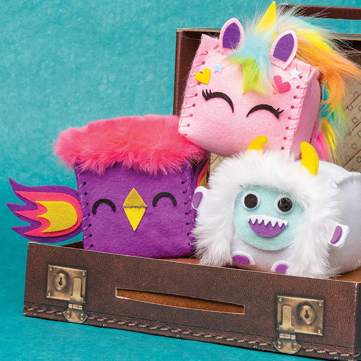 Lifestyle photo of some of the Sew Squishy Cubes all fully crafted and sitting in a paper suitcase. Critters include a purple bird, a pink unicorn, and a fuzzy yeti