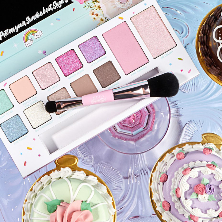 A Petite 'n Pretty makeup palette featuring sparkly pastel shades, laying open on a dessert table with a rose gold makeup brush laying on top of it