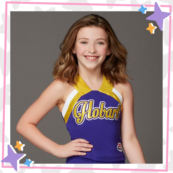 Kira McClure poses with her hand on her hip, smiling, and wearing her cheerleading uniform