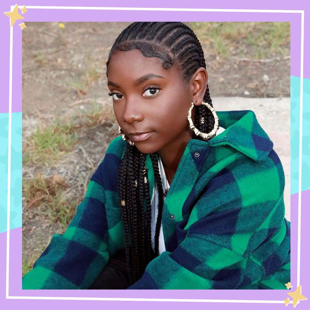 Photo of Kheris Rogers sitting outside wearing a green and blue flannel jacket and big gold hoop earrings