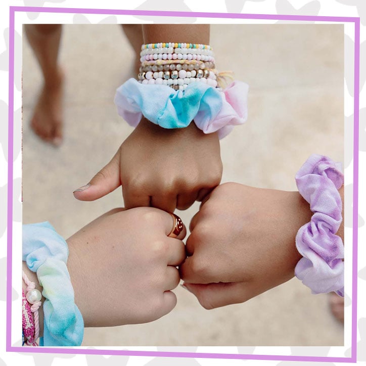 Lifestyle photo of three girls holding their fists together, showing off their house of neveRland custom dyed scrunchies