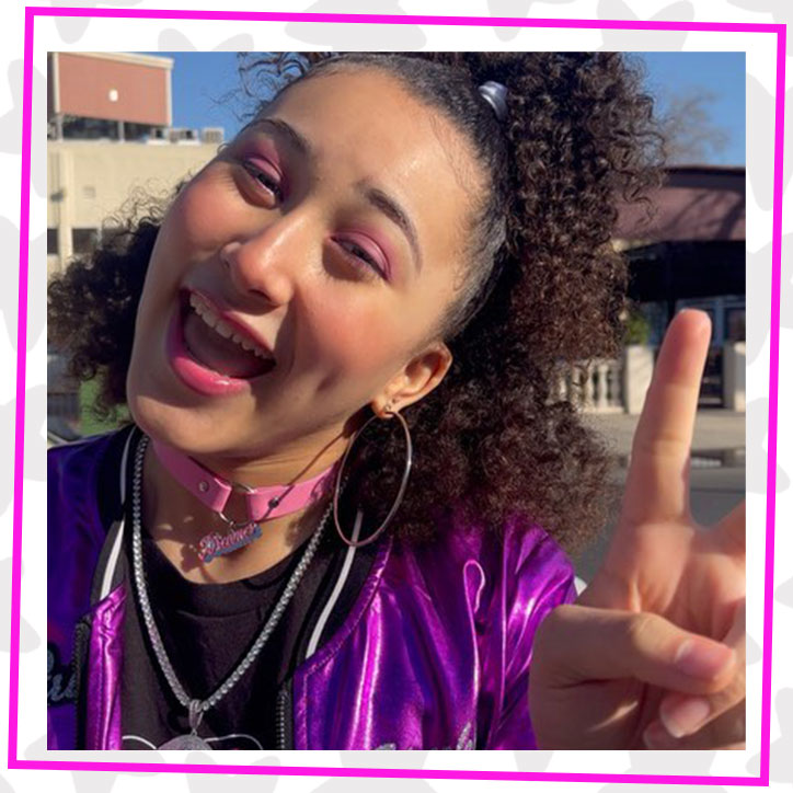 Sparkle getting ready to record the GLOTIVATION Rock Your GLO music video in her metallic purple GLOTIVATION bomber jacket. She is smiling and holding up a peace sign.