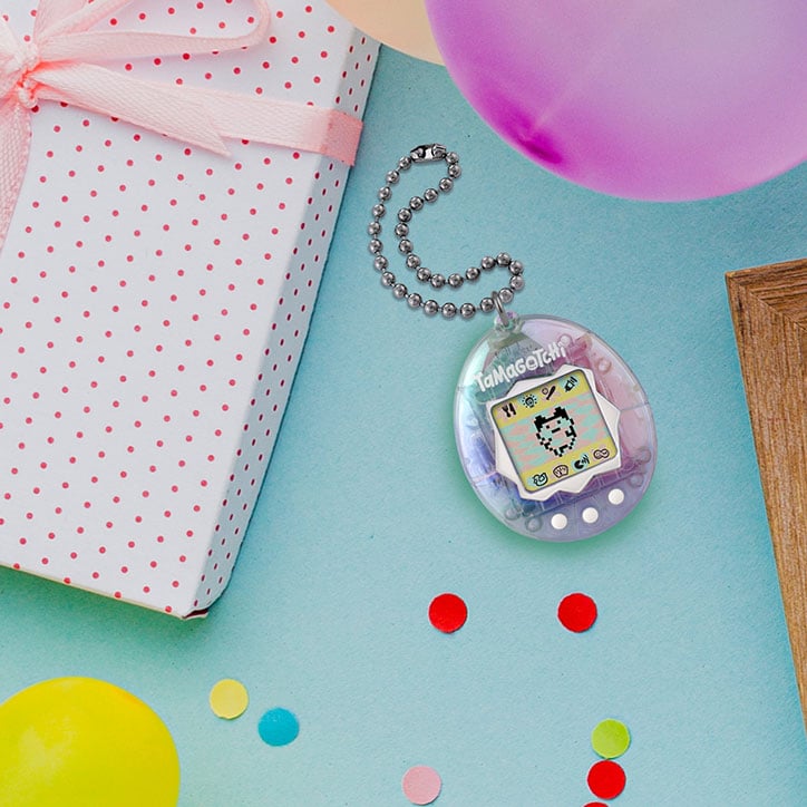 Flat Lay of the Original Tamagotchi 25th Anniversary device layed out with a wrapped gift, confetti, and a party balloon
