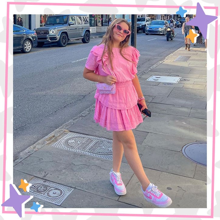 Maddy from JKrew posing in a ruffly pink dress and pink sunglasses on a city street