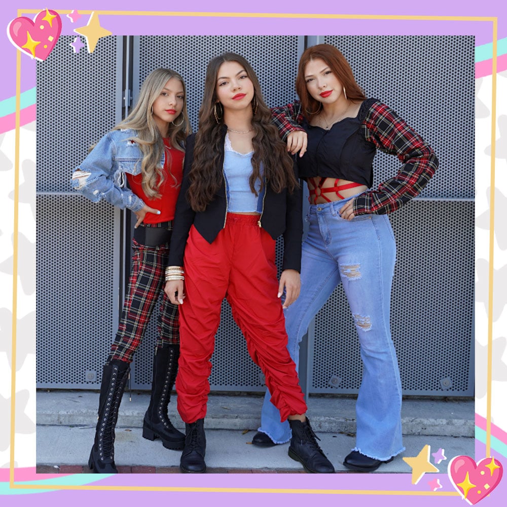 Gabriella, Raena, and Amalia from Triple Charm pose in coordinating red, black, plaid, leather, and denim fall outfits in front of a metal fence