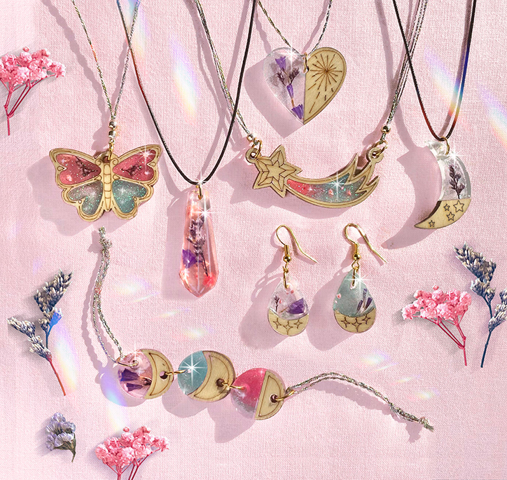Lifestyle photo of some of the necklaces, bracelets, and earrings you can make with the Wish*Craft Wood & Resin Charm Jewelry kit, including charms shaped like butterflies hearts, moons, and stars