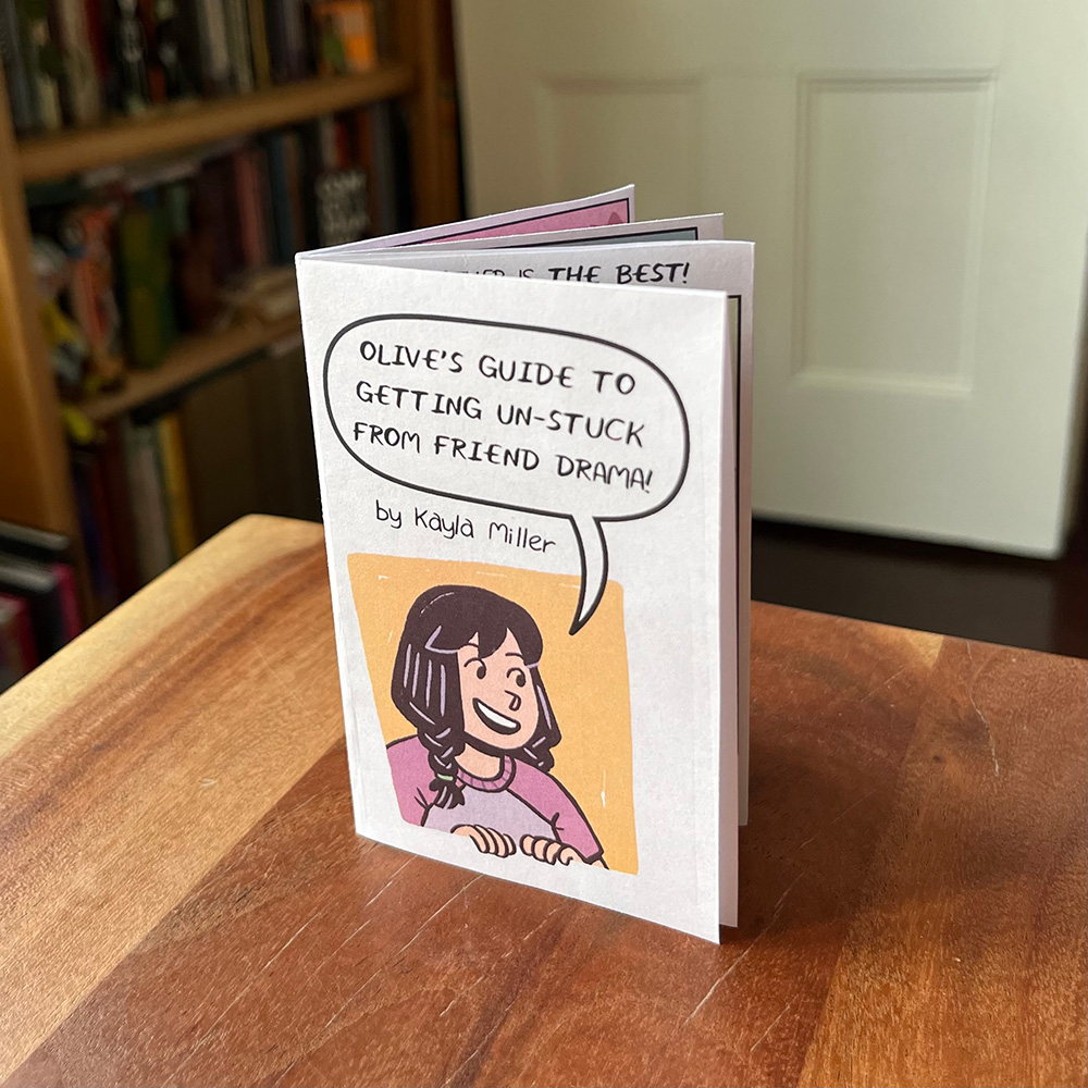 A printed, folded zine-style version of the Stuck minicomic standing on a wooden table